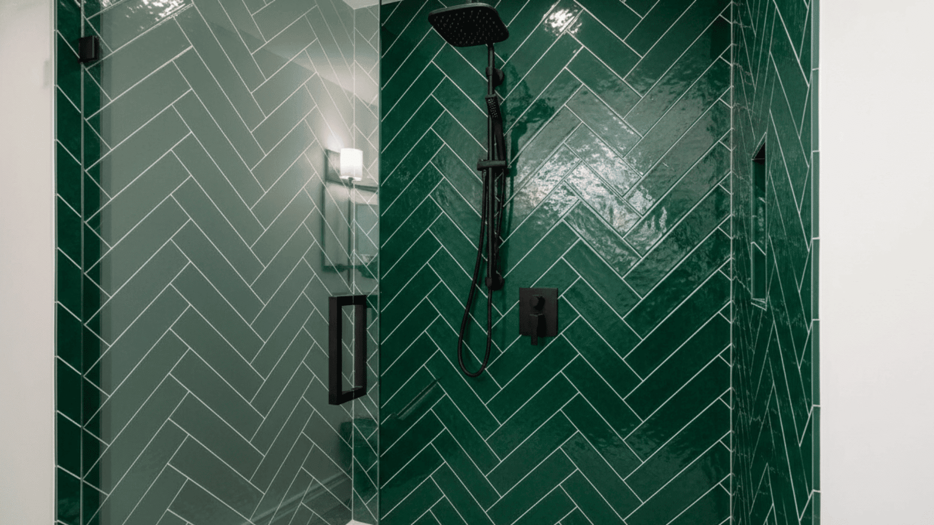 Green herringbone pattern shower tiles with black fixtures and a glass door.