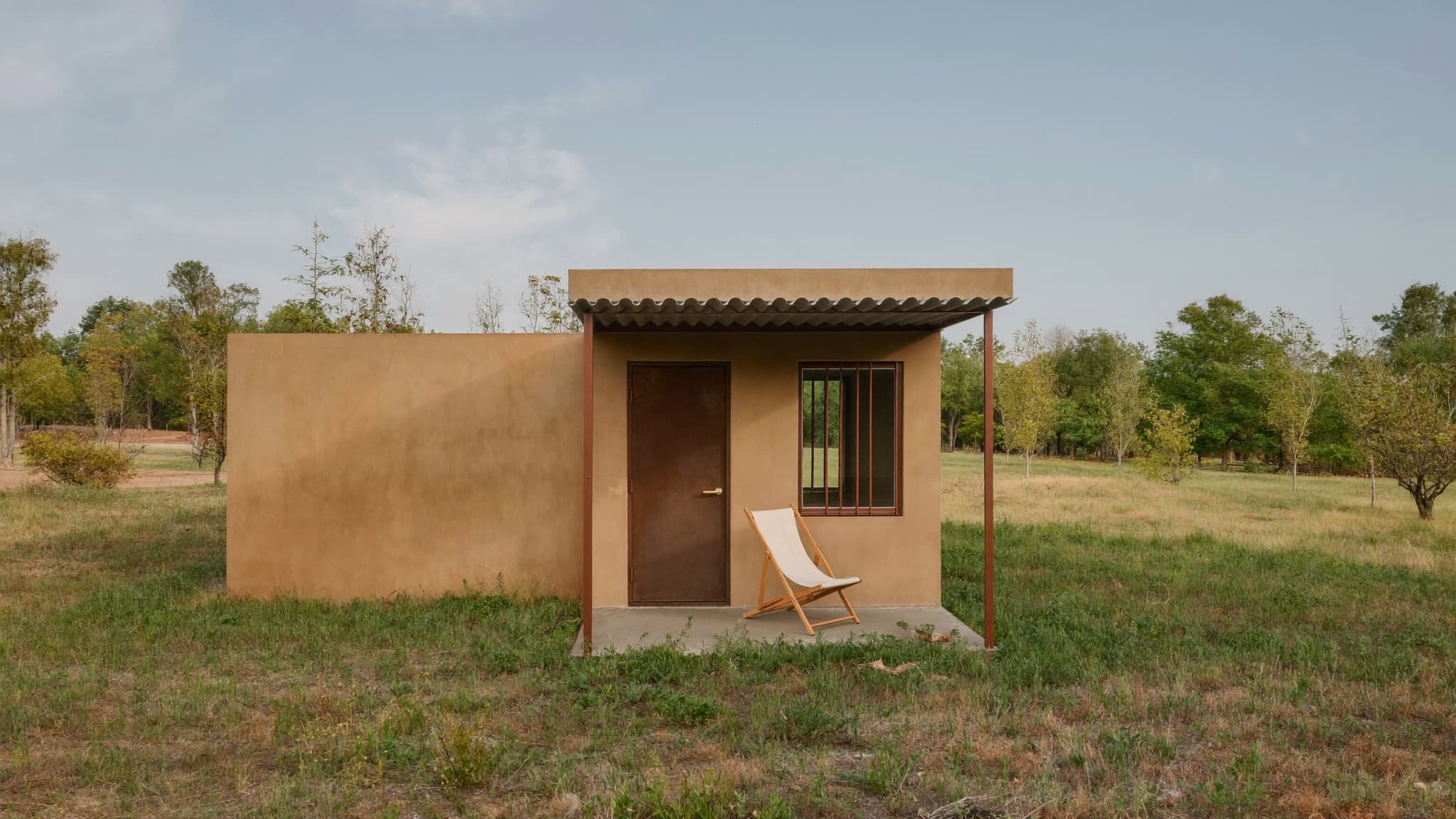 A compact wooden tiny house on a trailer situated in a natural landscape.