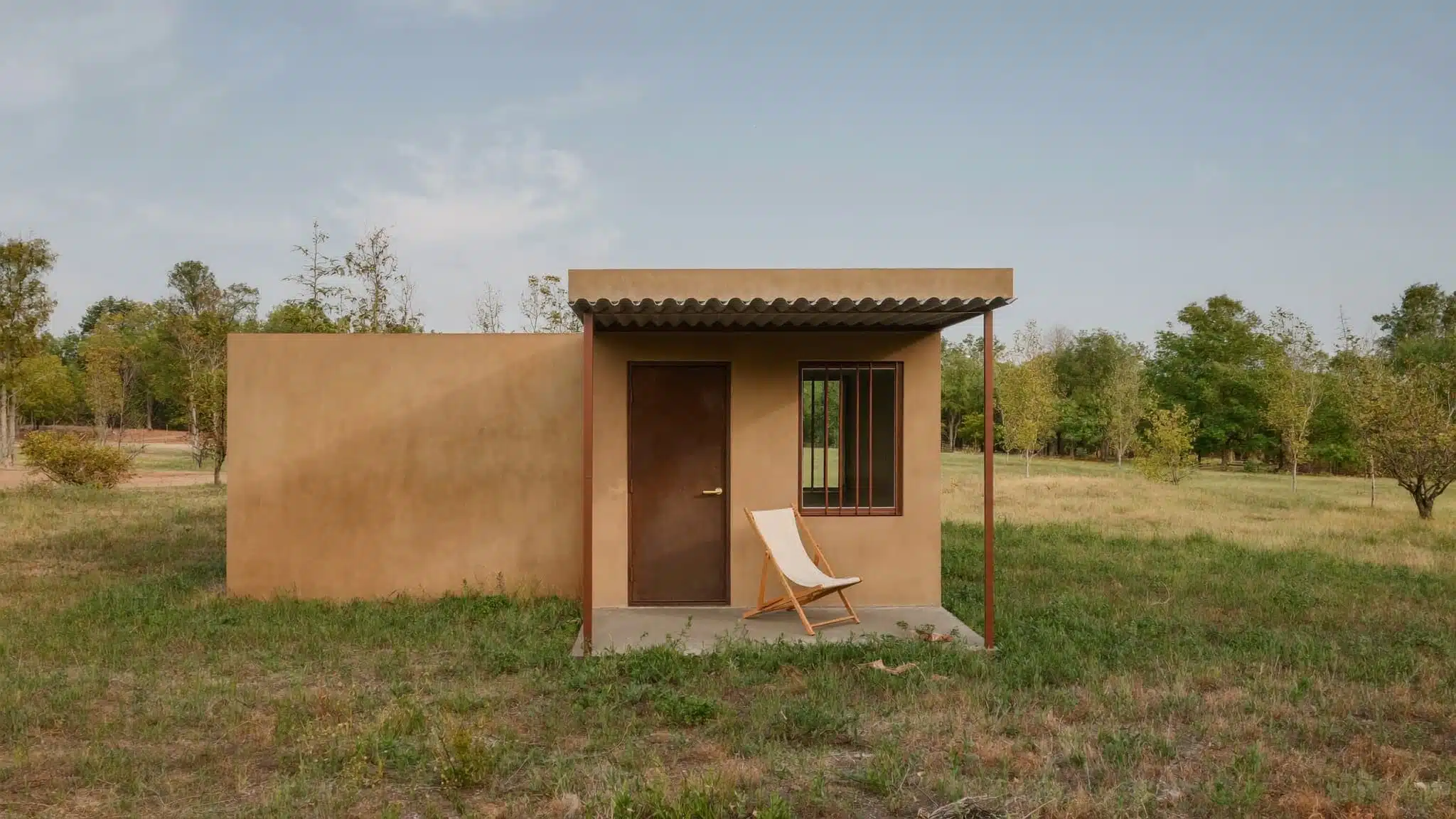 A compact wooden tiny house on a trailer situated in a natural landscape.