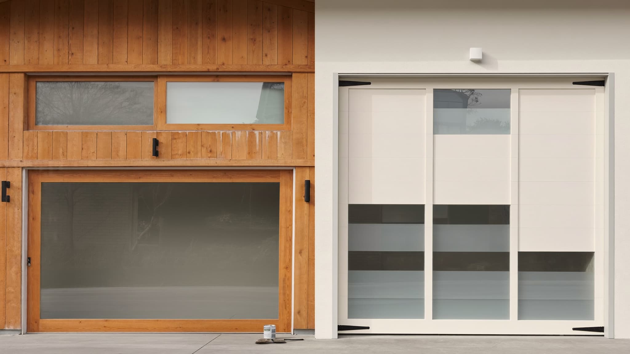 Side-by-side view of two garage doors: a warm wood carriage-style door and a modern white flat-panel door with window panels.