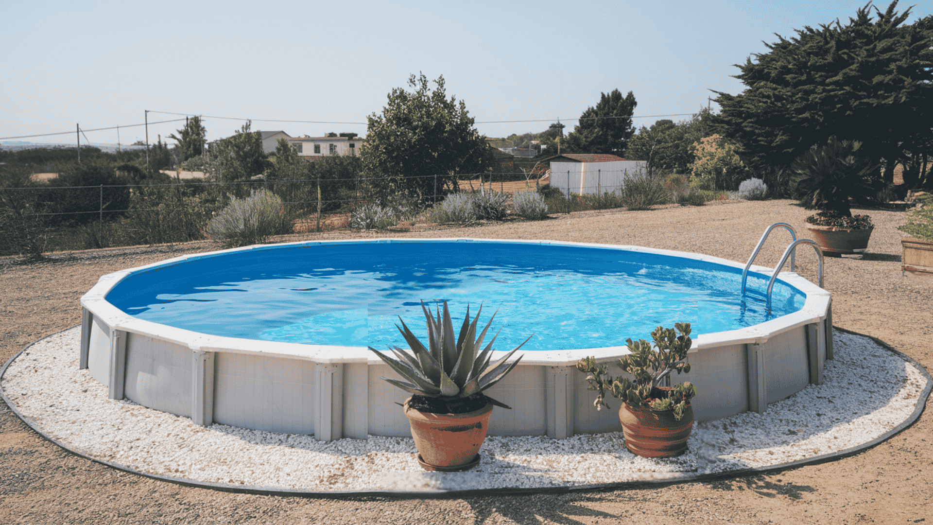 Round above-ground swimming pool with gray paneled walls, surrounded by white gravel landscaping and an integrated pool ladder.