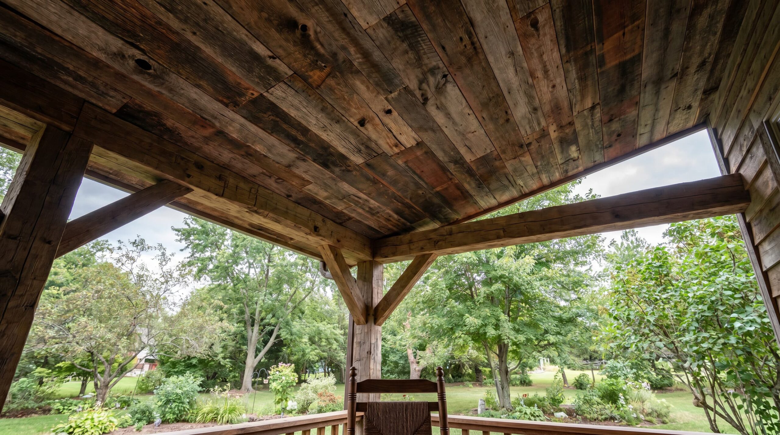 Covered porch with rustic wooden ceiling, large supporting beams, and lush garden view.
