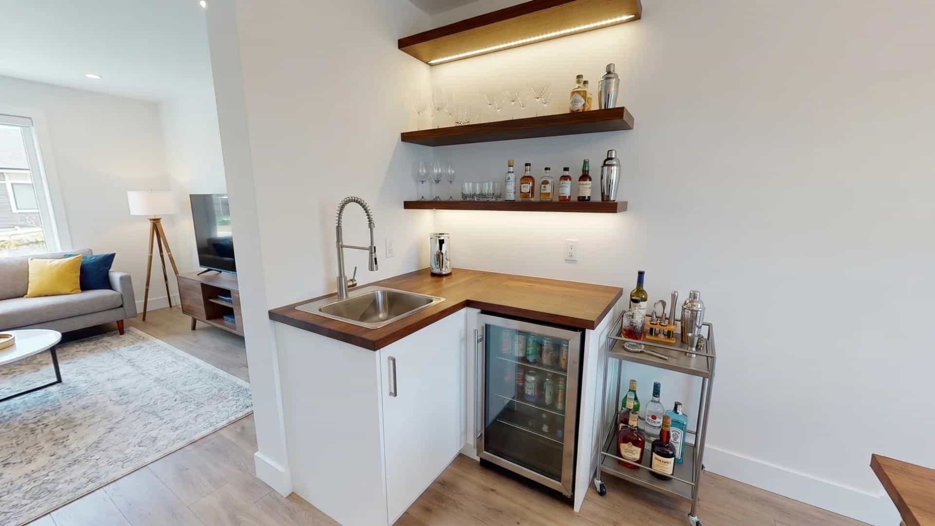 Compact wet bar with floating shelves, mini fridge, and wood countertop in small living space.