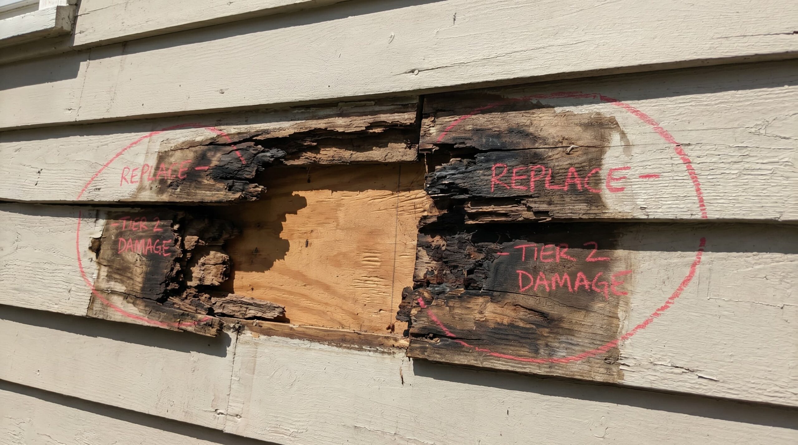 An image showing structural damage to wood siding, with rot and warping affecting one or two boards, but the underlying sheathing remains intact.