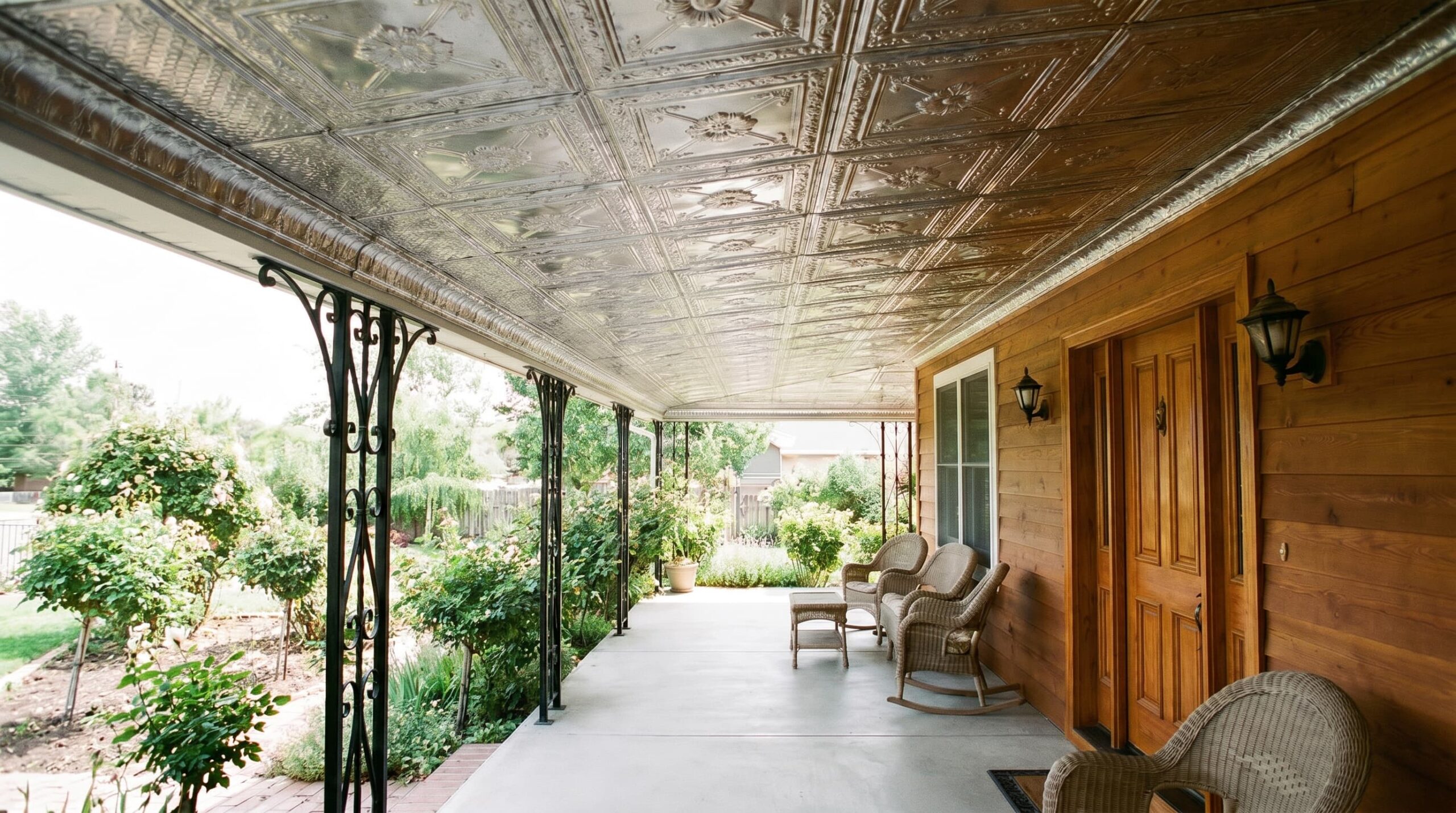 Covered porch with decorative tin ceiling, wooden walls, wicker chairs, and garden view.