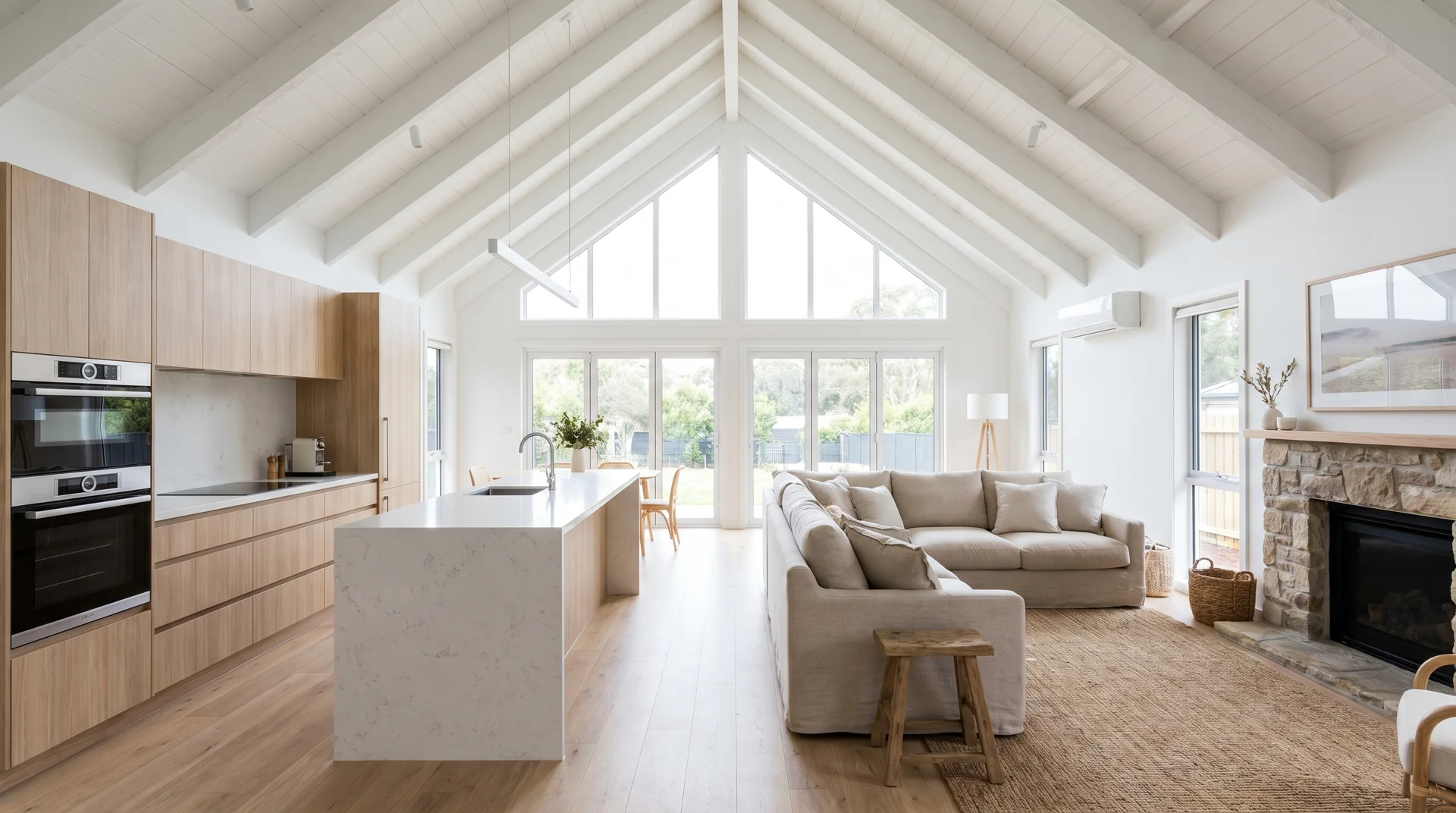 Open-concept home with a white vaulted ceiling, a marble kitchen island, and a beige sofa next to a stone fireplace.