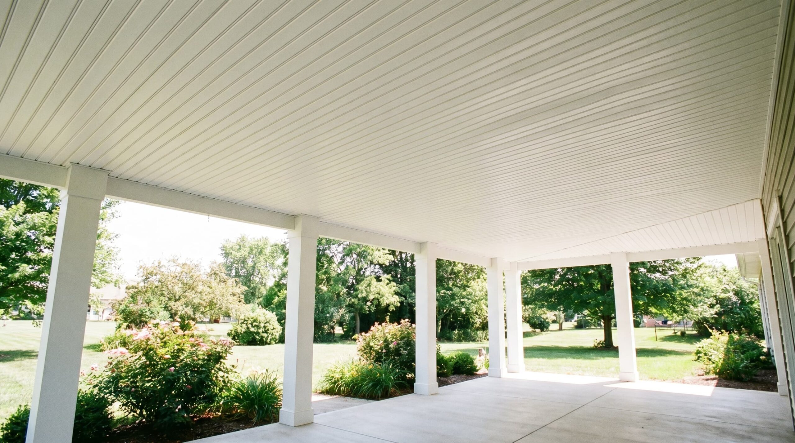 Covered porch with white beadboard ceiling, supporting columns, and landscaped garden view.