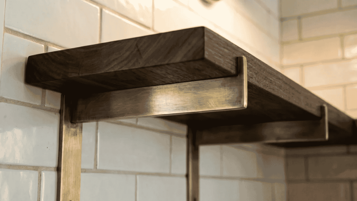 Floating dark wood bathroom shelf with metal brackets mounted on white subway tile wall, minimal modern style