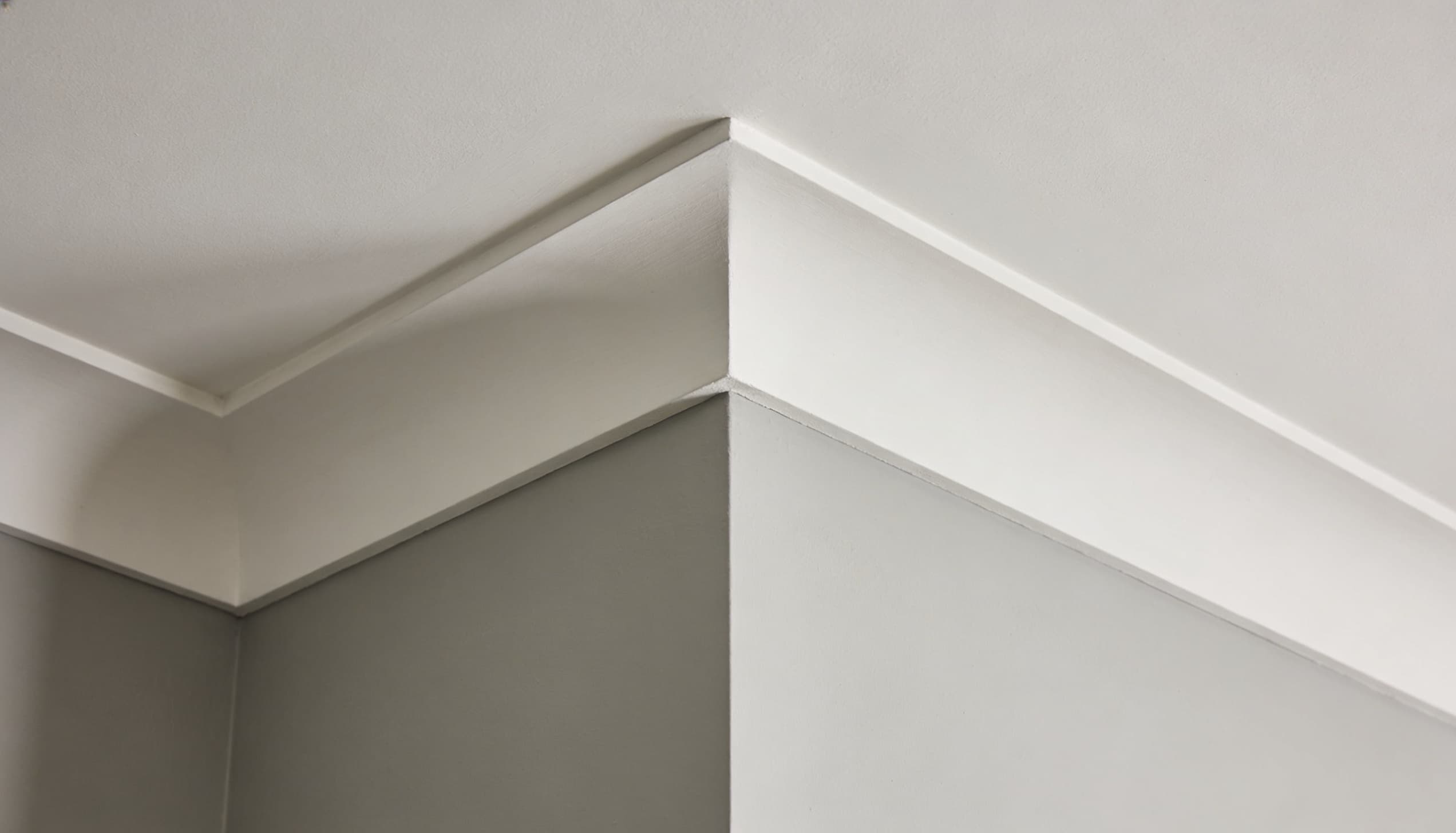 Simple white cove crown molding with a smooth, concave curve installed at the corner of a white wall and ceiling.