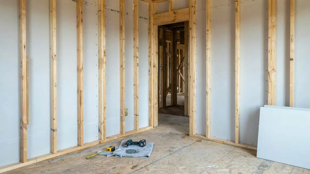 Interior construction scene showing 1/2 inch drywall installed on wall framing with exposed studs, emphasizing standard residential wall application and structural alignment.