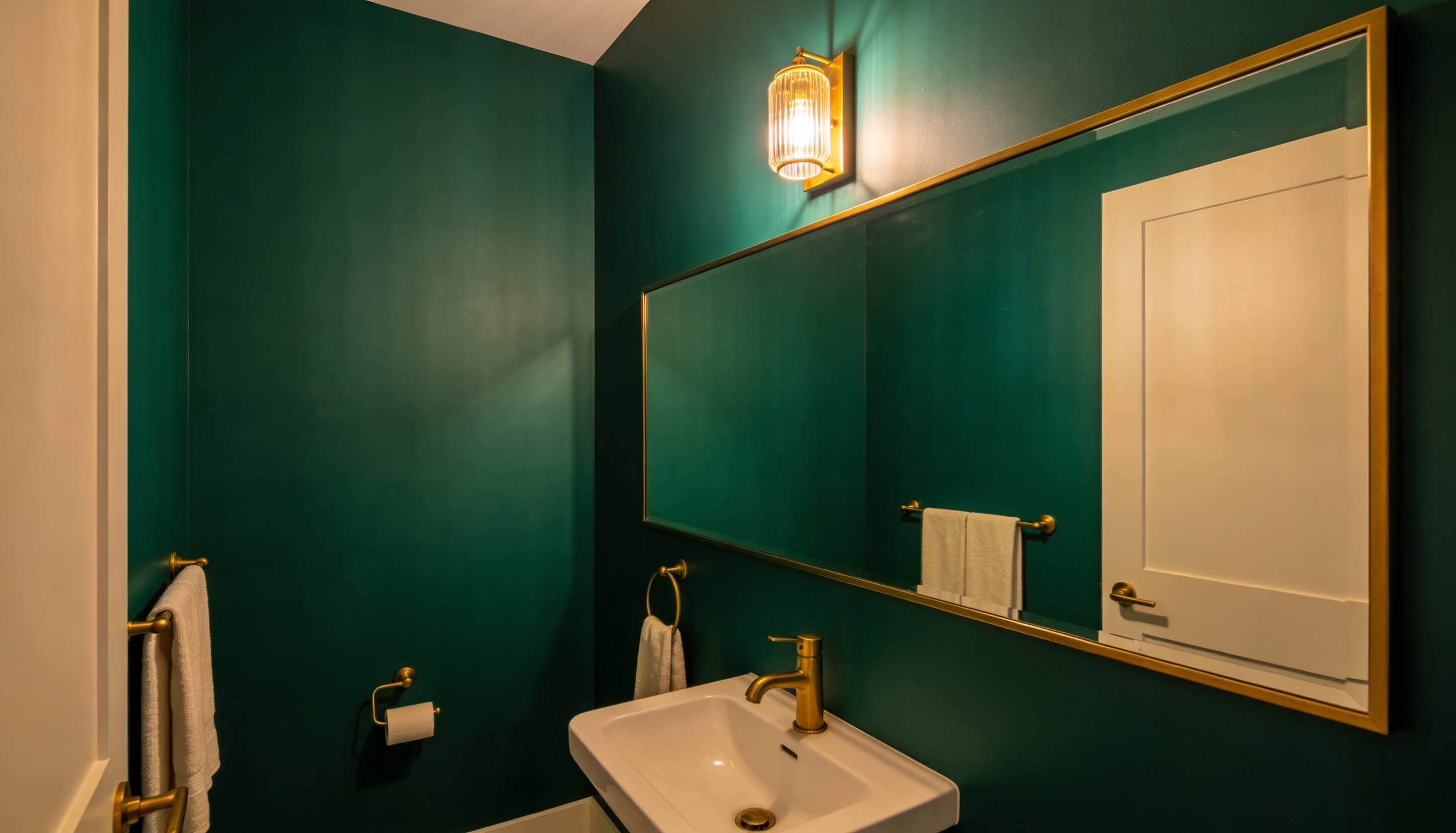 Bathroom with deep jewel-toned green walls, gold fixtures, and a white sink, creating a luxurious and intimate atmosphere.