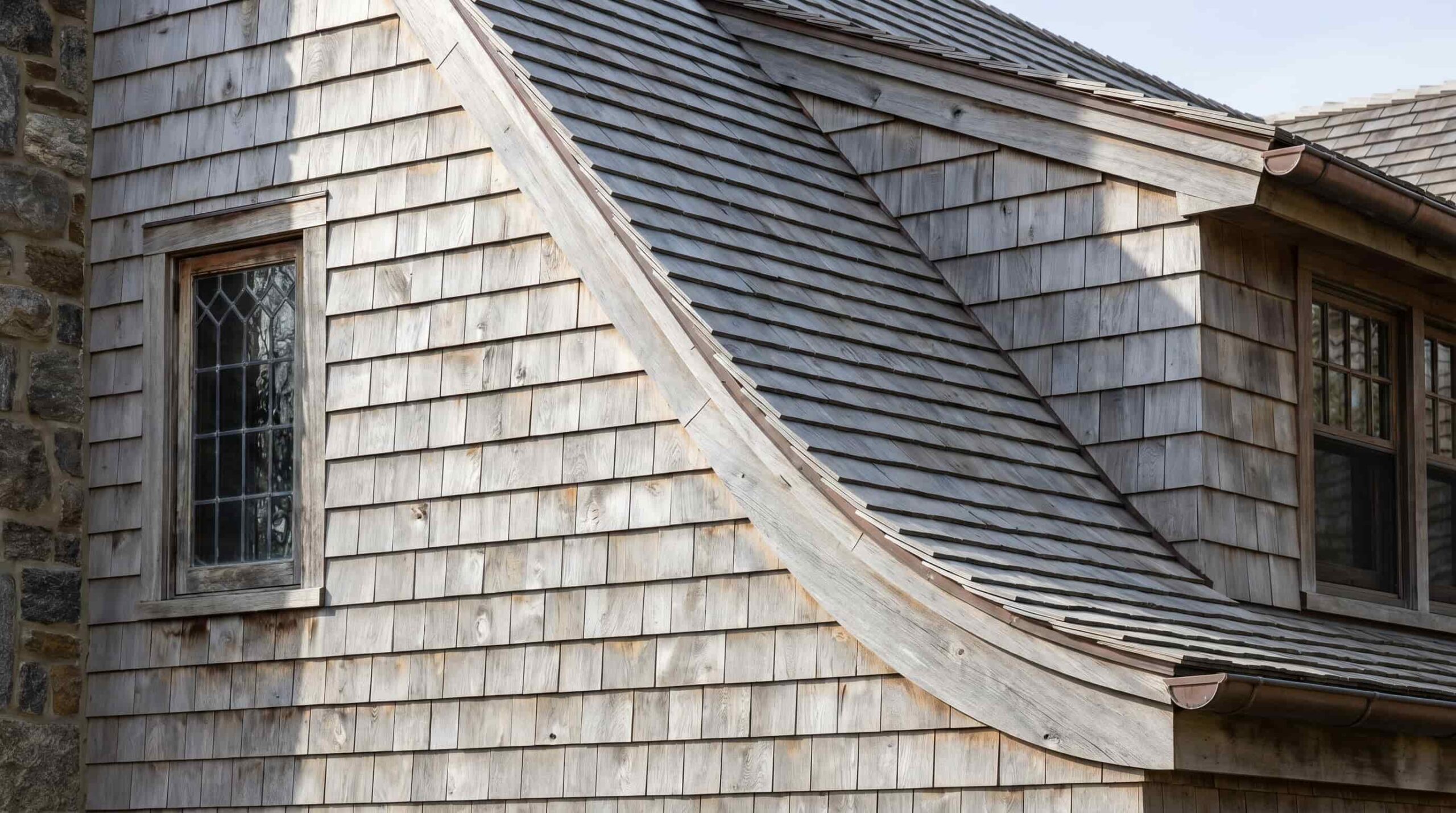 Close-up of a cedar shingle exterior with a curved roofline and small window detail
